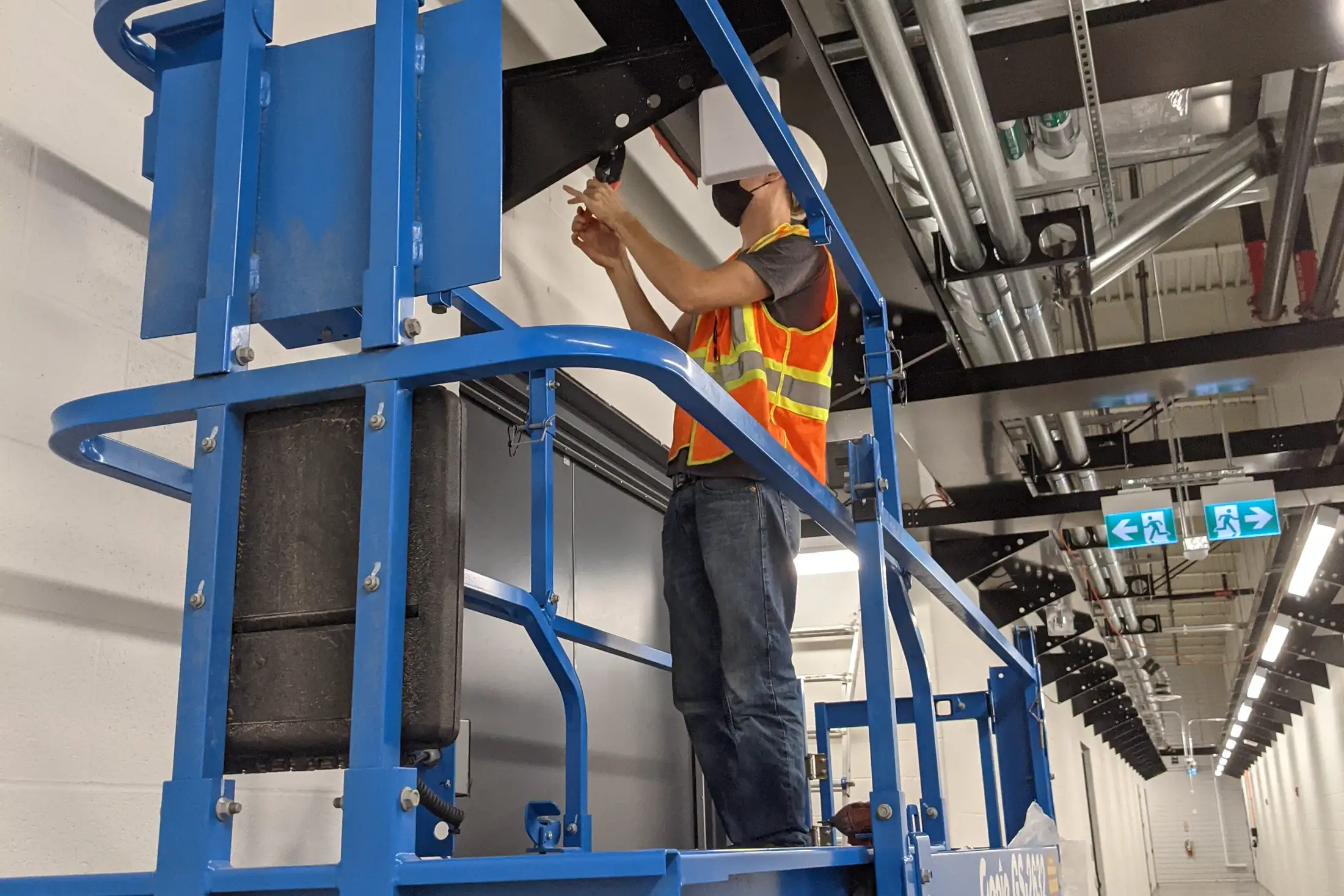 Installer on a scissor lift fitting an indoor antenna to the ceiling of a commercial corridor.